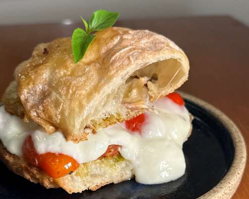 Sanduíche de focaccia com mussarela derretida, tomate cereja e manjericão